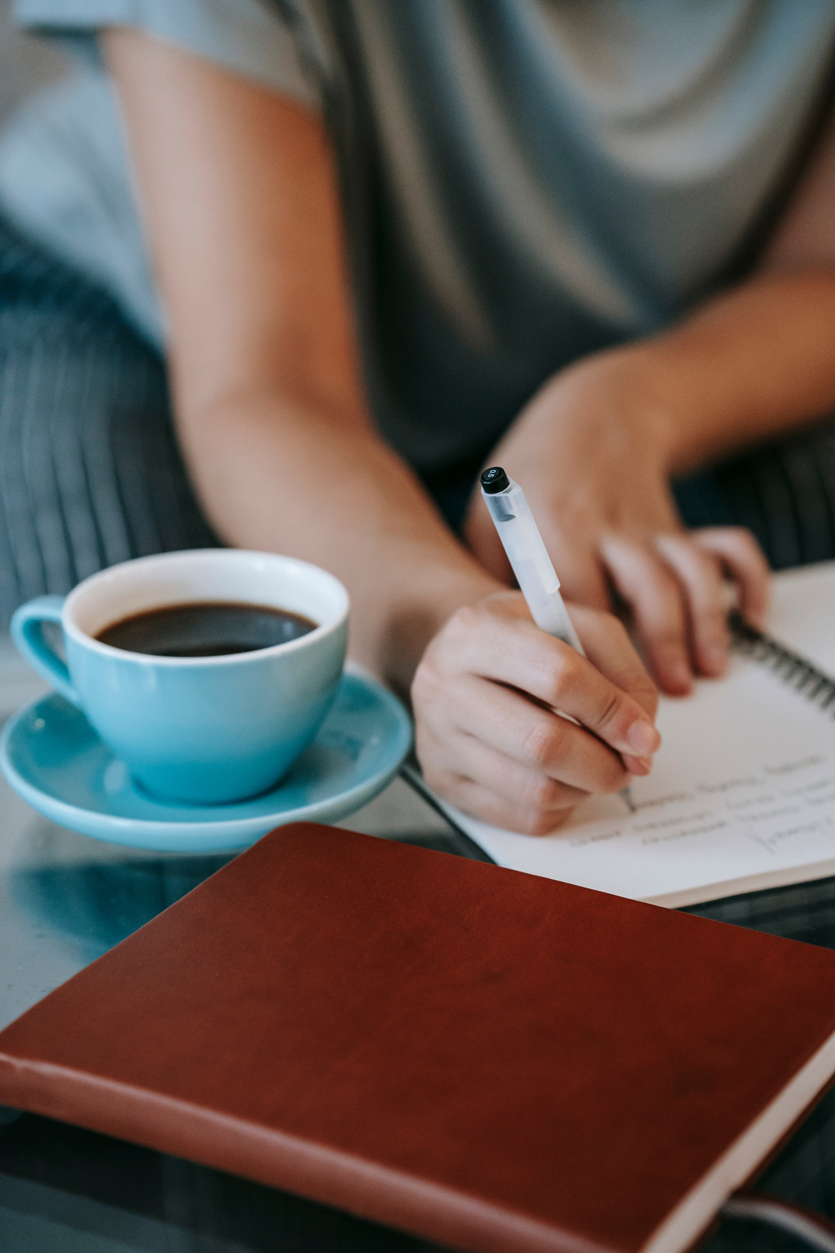 Faceless female journalist writing in notebook and drinking coffee